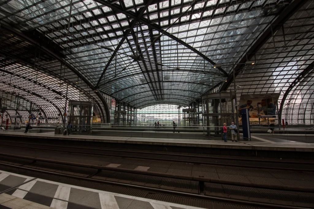 Des voyageurs attendent sur les quais de la gare centrale de Berlin, sous une grande verrière de verre et d’acier.